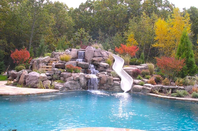 Beecher A - Wall, NJ - A swimming pool with a waterfall and a slide surrounded by colorful trees