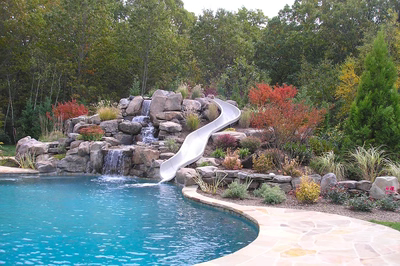 Beecher B - Wall, NJ - A swimming pool with a waterfall and a slide surrounded by lush greenery