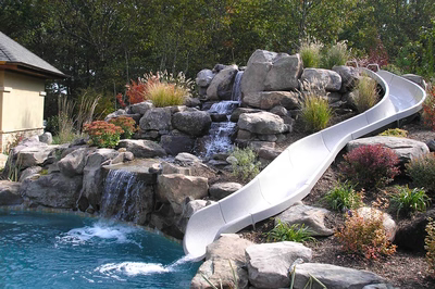 Beecher E - Wall, NJ - A large rock pool with a water feature and a slide, surrounded by lush greenery