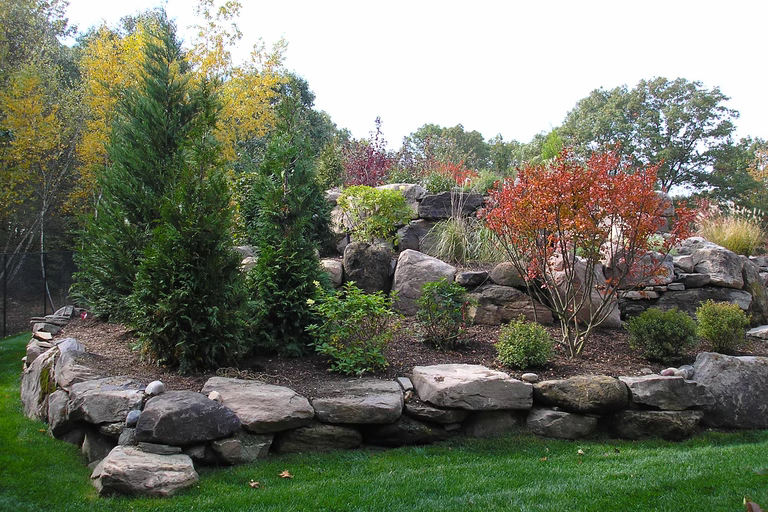 Natural stone boulder waterfall cascading through lush greenery and colorful autumn shrubs