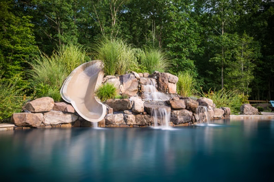 Belden C - Williamstown, NJ - A water feature with a water slide in the middle of a swimming pool surrounded by lush greenery