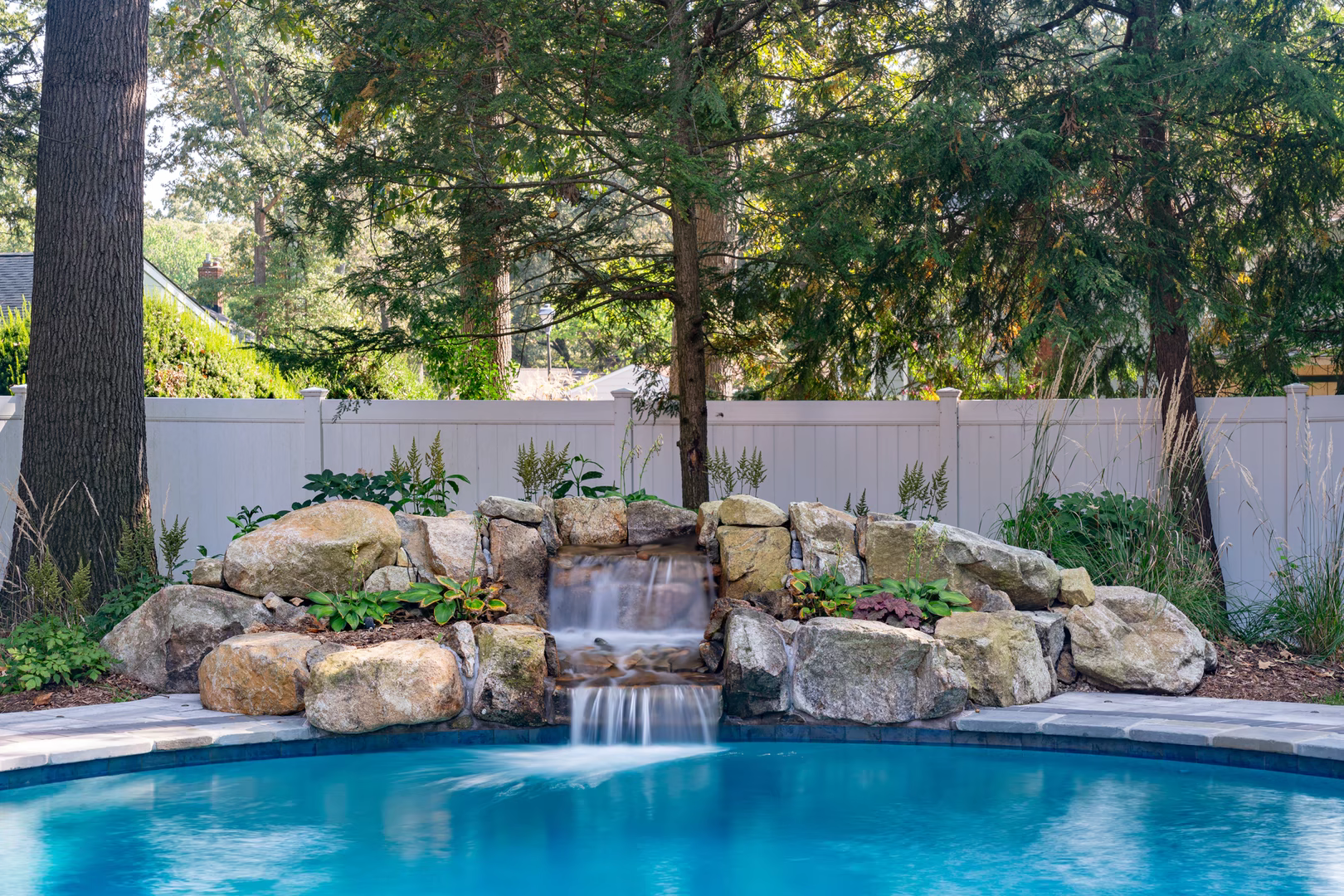 Natural stone boulder waterfall cascading into a pool surrounded by lush green plants