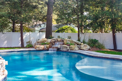 Belding G - Queenstown, MD - A swimming pool with a waterfall in the middle surrounded by trees and a white fence