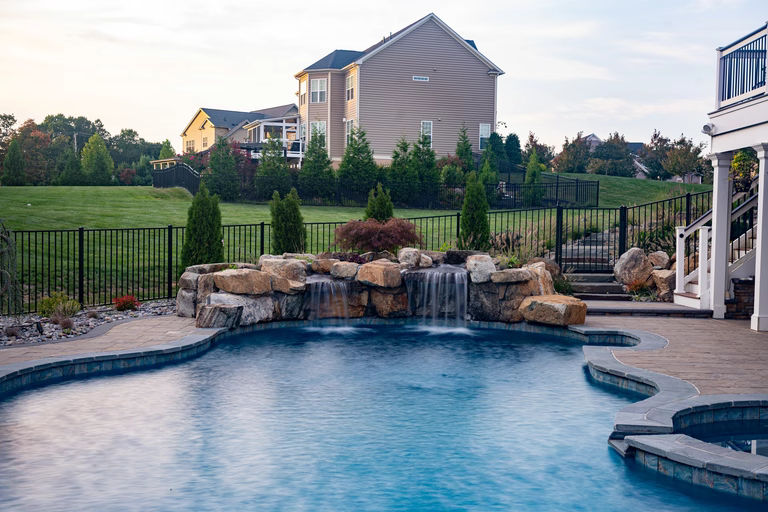 Natural stone boulder waterfall cascading into a backyard pool with lush landscaping