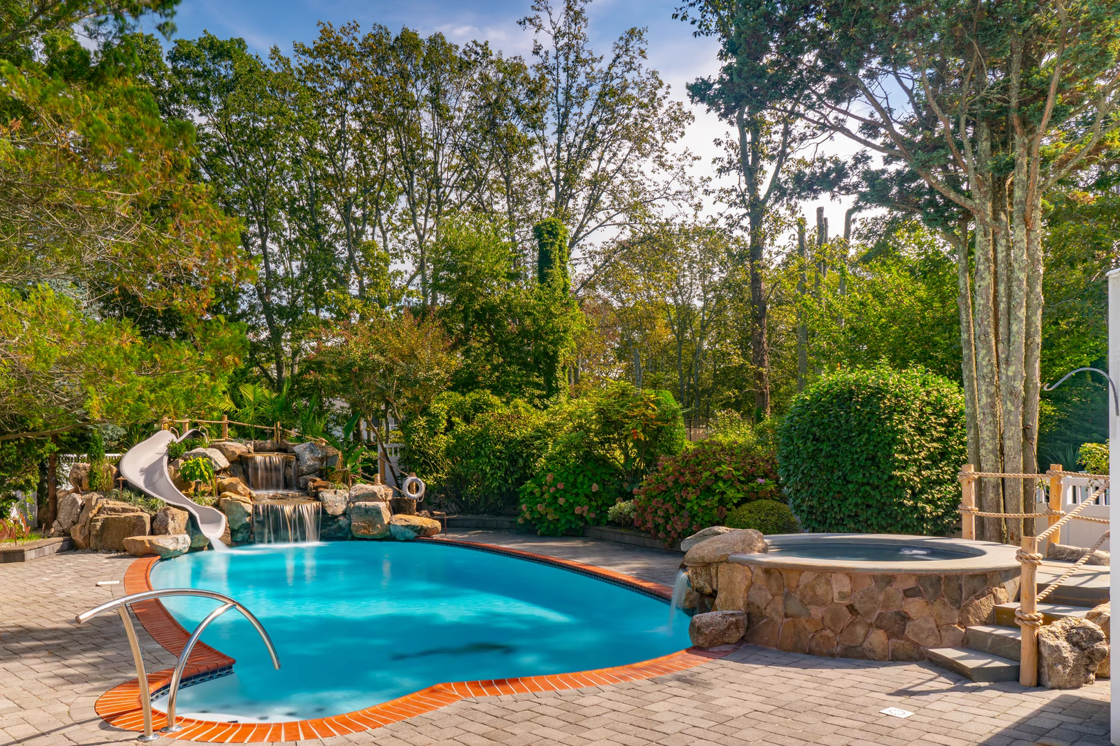 Two-tiered natural stone boulder waterfall cascading into a pool surrounded by lush garden plants