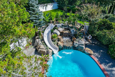 Benham K - Cape May Courthouse, NJ - A swimming pool with a water feature and a slide surrounded by lush greenery