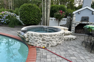 Benham M - Cape May Courthouse, NJ - A pool with a fire pit and a fire place next to it surrounded by lush greenery and flowers