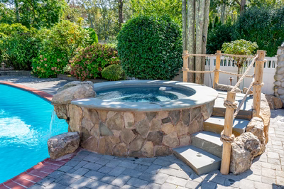 Benham N - Cape May Courthouse, NJ - A swimming pool with a hot tub surrounded by lush greenery and rocks
