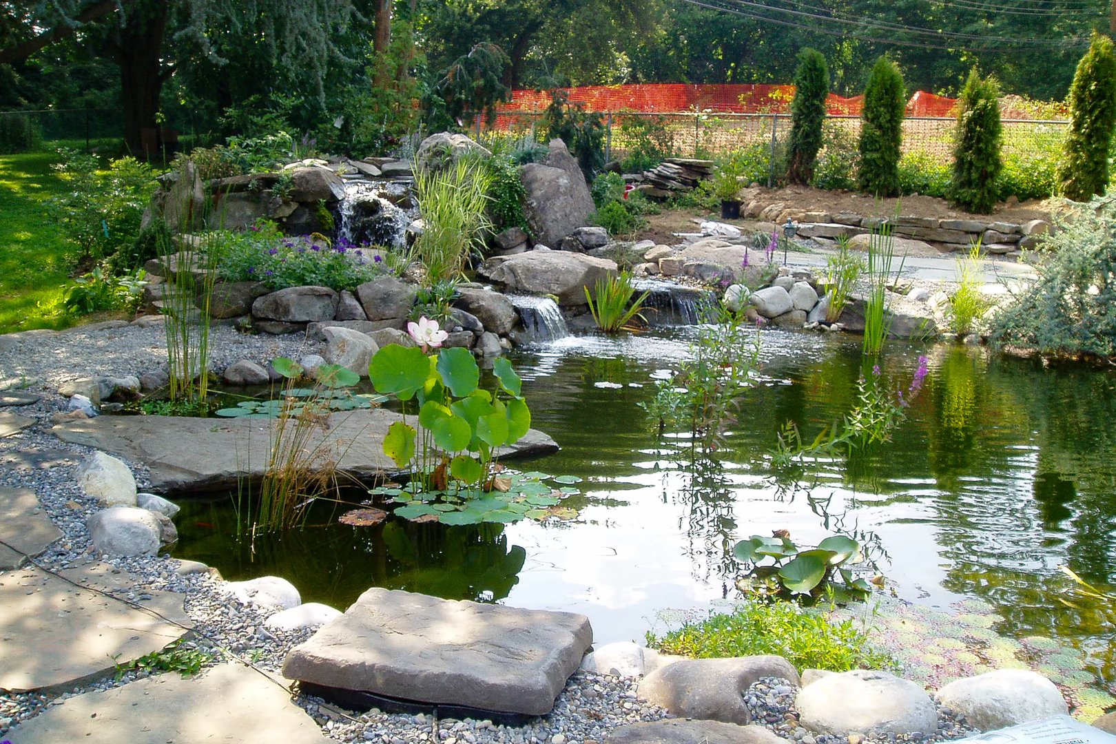 Multi-tiered natural stone boulder waterfalls cascading into a garden pond with lush aquatic plants