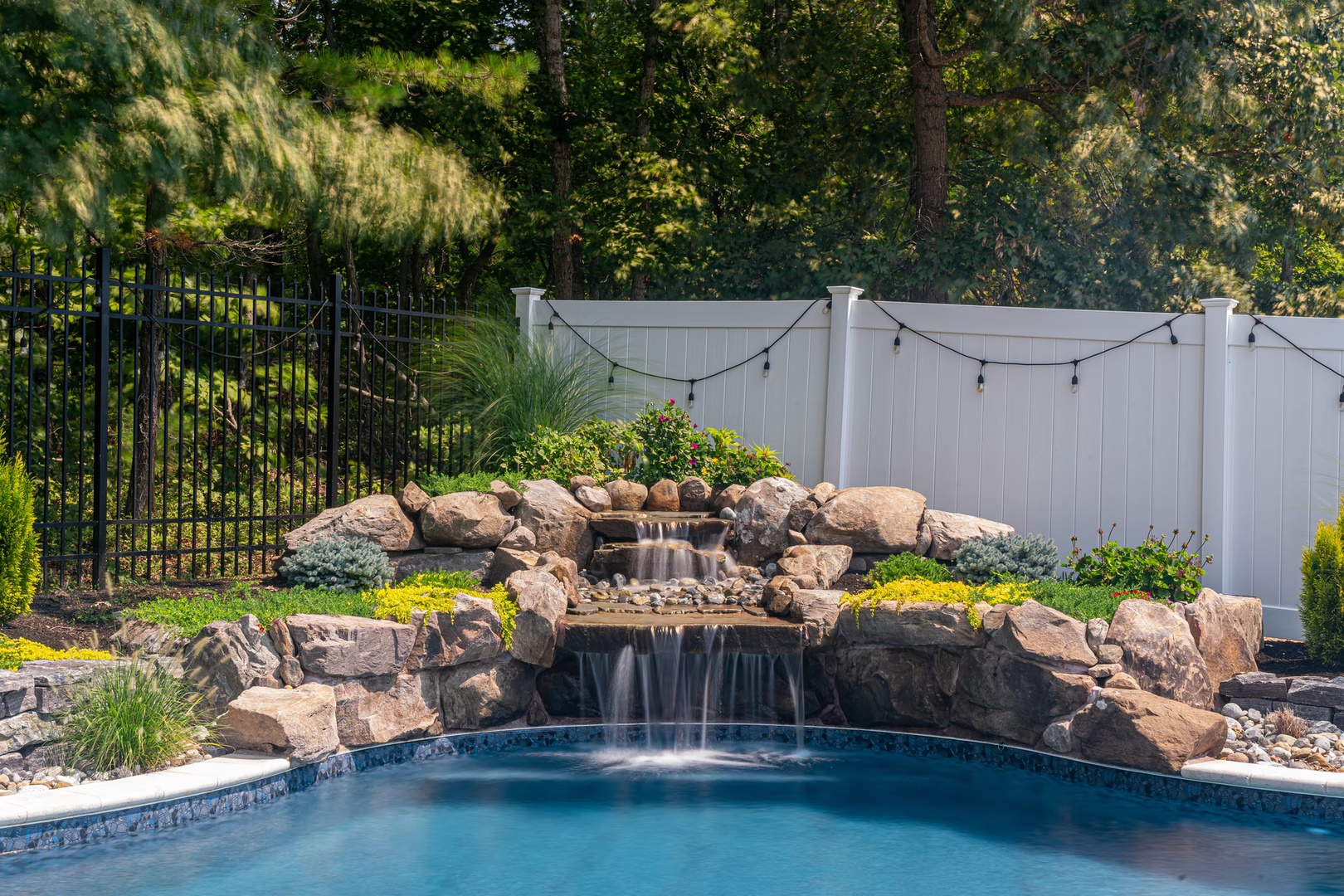 Two tiered natural stone boulder waterfall cascading into a pool with lush garden landscaping