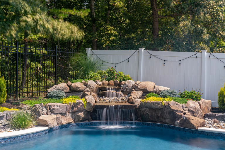 Natural stone boulder waterfall cascading into a pool with lush garden landscaping