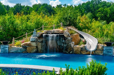 Berlin E - Robbinsville, NJ - A swimming pool with a waterfall and a water slide surrounded by lush greenery