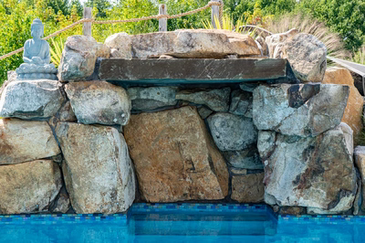 Berlin G - Robbinsville, NJ - A stone structure with a seated buddha statue in the middle of a swimming pool surrounded by lush greenery