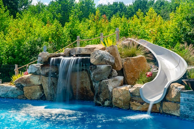 Berlin H - Robbinsville, NJ - A swimming pool with a waterfall and a slide surrounded by lush greenery