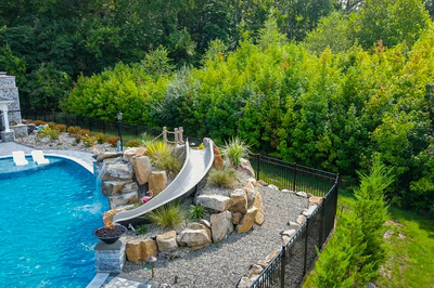 Berlin K - Robbinsville, NJ - A backyard with a pool and a water slide surrounded by lush greenery
