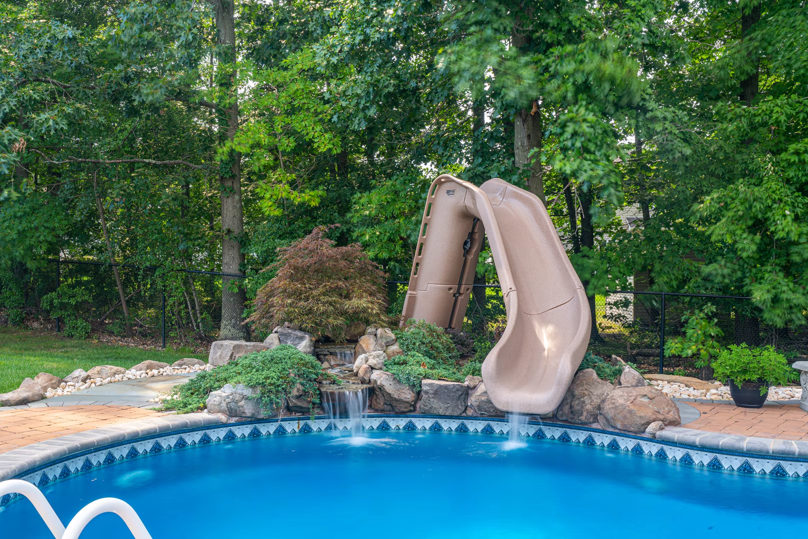 Two-tiered natural stone boulder waterfall cascading into a blue pool surrounded by lush greenery