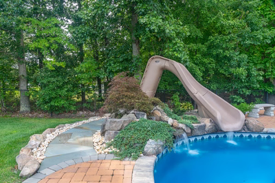 Blackwater G - Monroe, NJ - A backyard with a pool and a water slide surrounded by lush greenery