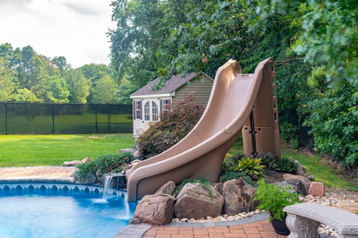 Blackwater J - Monroe, NJ - A backyard with a water slide and a pool surrounded by lush greenery