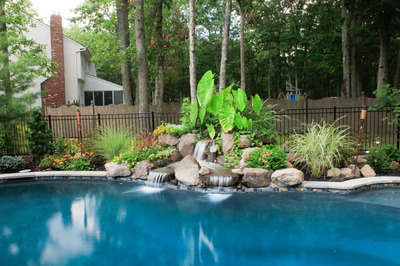 Bowman A - Medford, NJ - A backyard with a swimming pool surrounded by lush greenery and a waterfall
