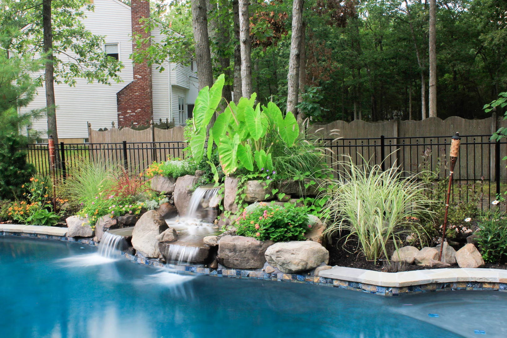 Multi-tiered natural stone boulder waterfall cascading into a pool surrounded by lush tropical plants