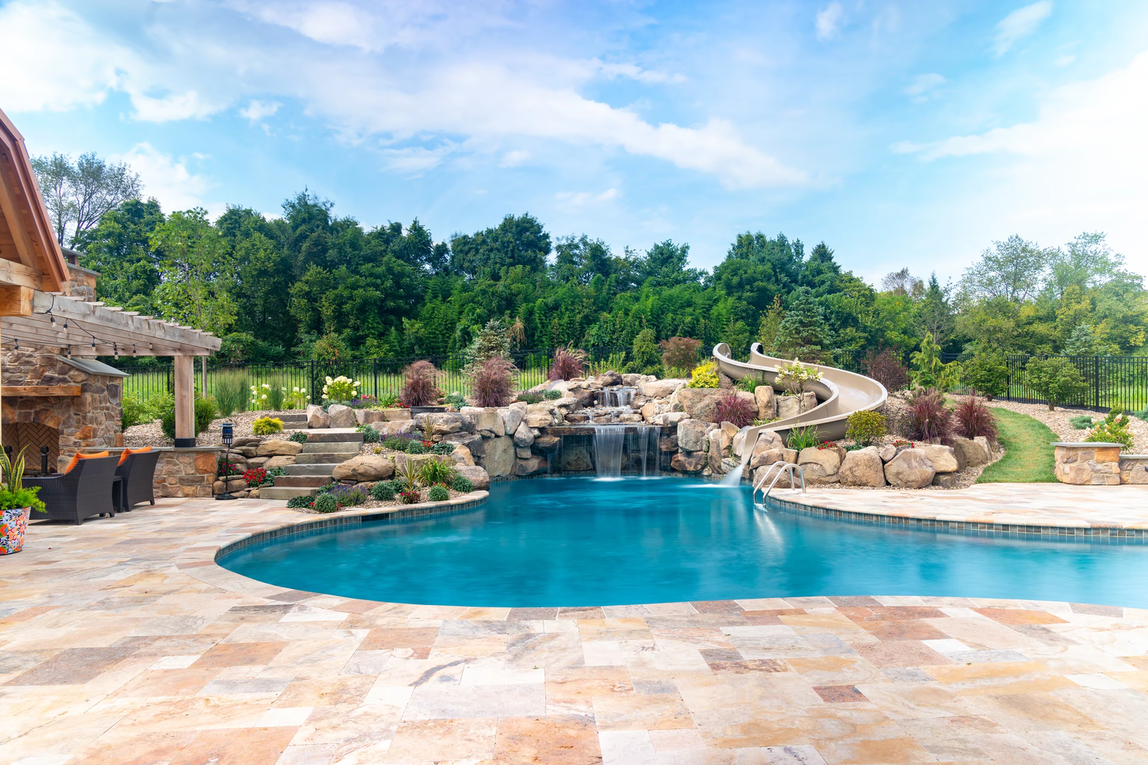 Two-tiered natural stone boulder waterfall cascading into a freeform pool with lush garden plants