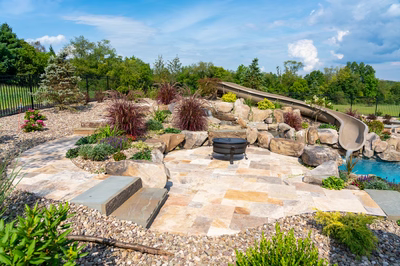 Bridge H - Lewisburg, PA - A backyard with a water feature and a fire pit surrounded by plants and rocks