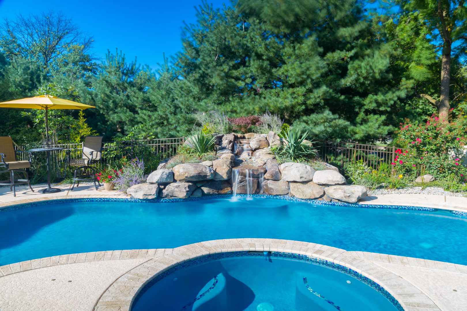 Natural stone boulder waterfall cascades into a freeform pool bordered by lush greenery