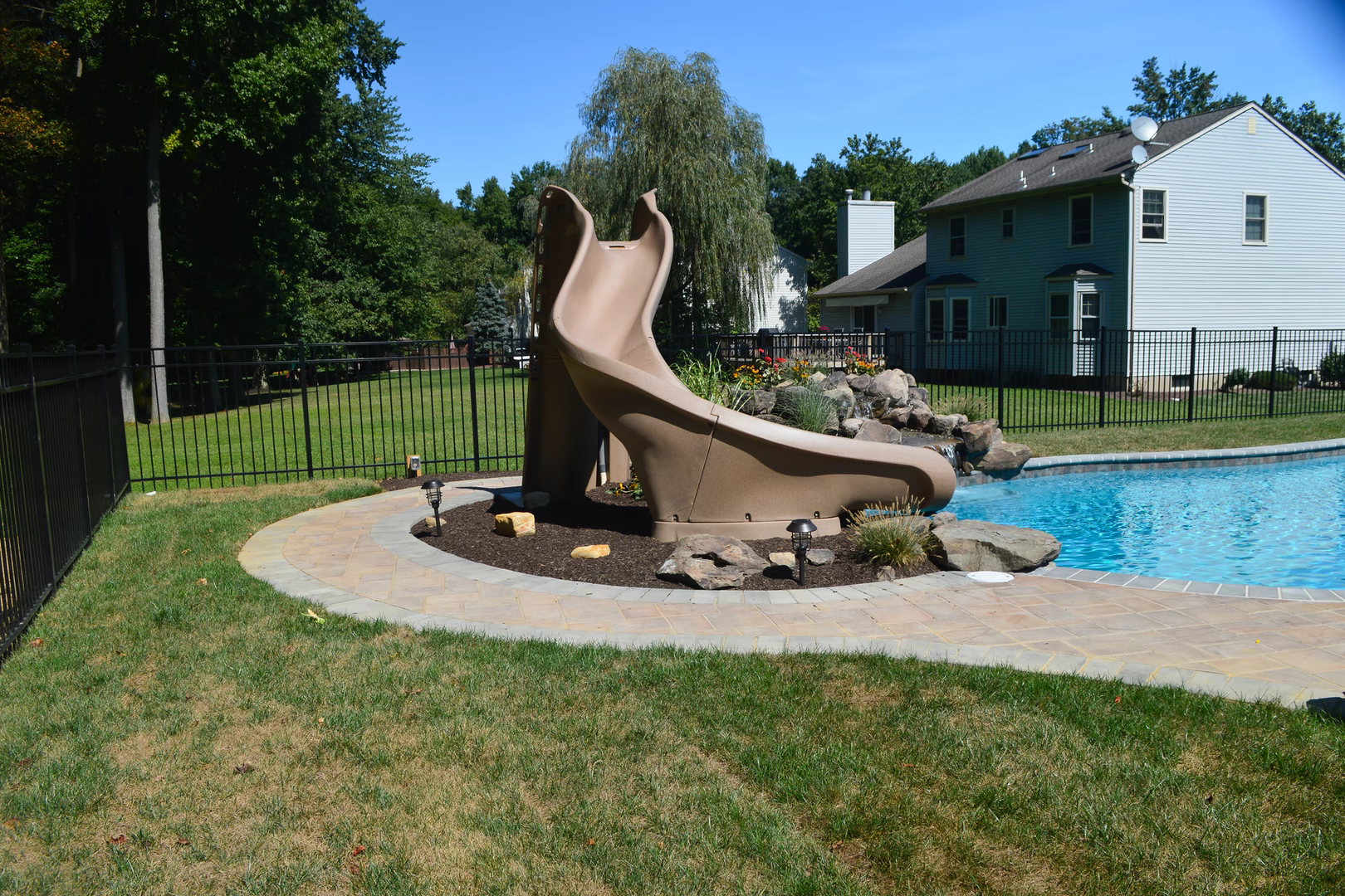 Natural stone boulder waterfall cascading into a swimming pool beside lush garden plants