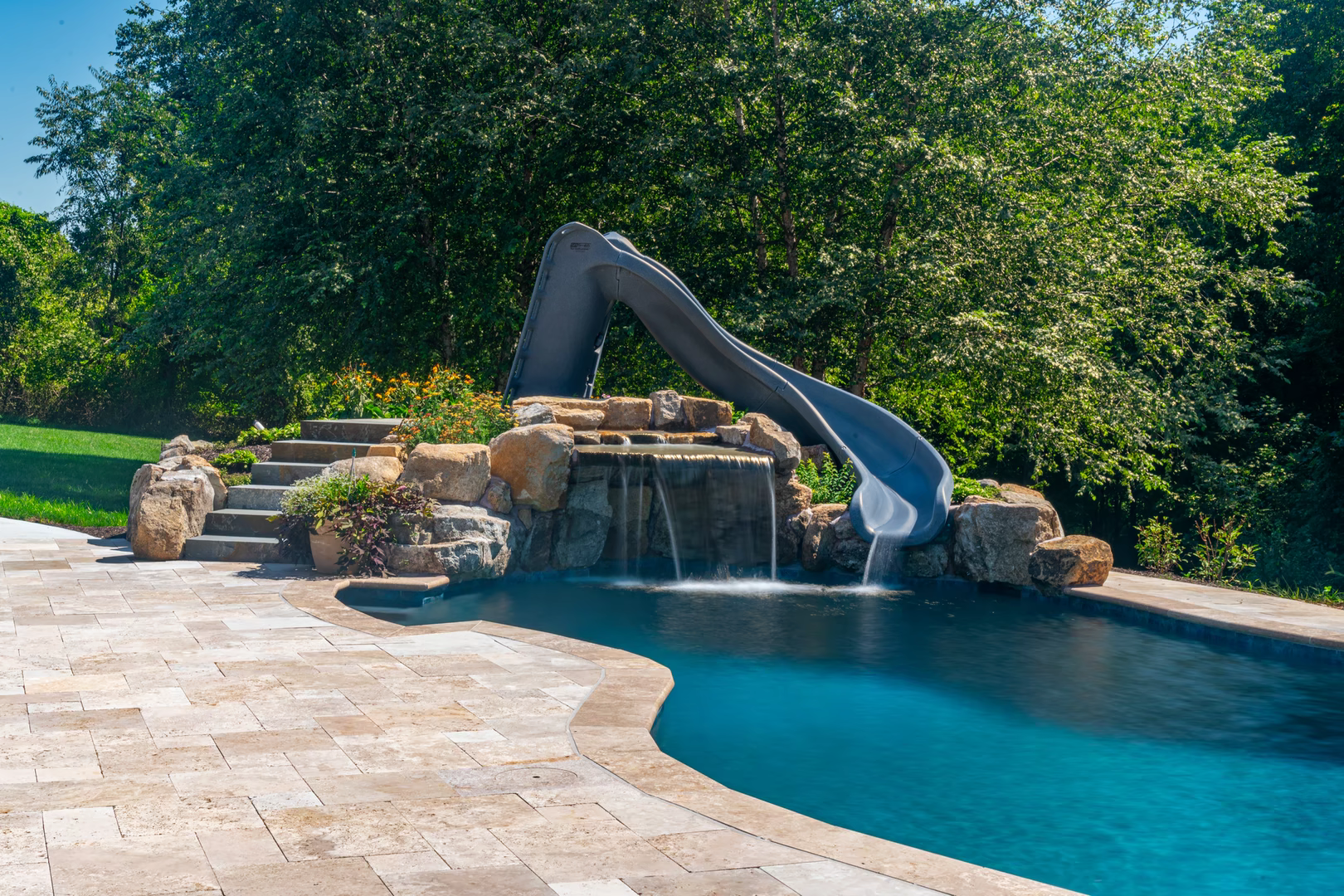 Natural stone boulder waterfall cascading into a pool with slide and lush landscaping