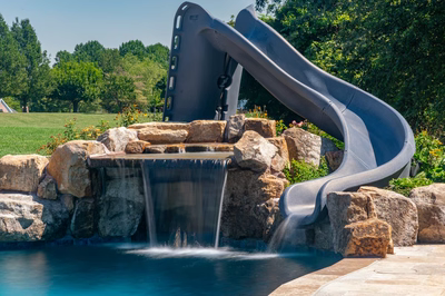 Burney - Matawan, NJ - A large blue water slide in the middle of a swimming pool surrounded by rocks and greenery