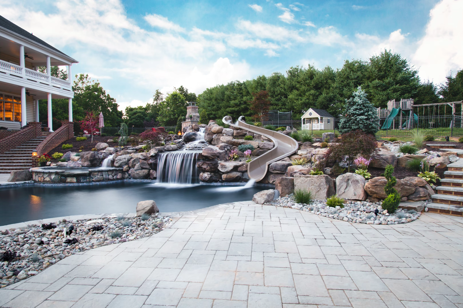 Multi-tiered natural stone boulder waterfall cascading into a dark pool with lush garden landscaping