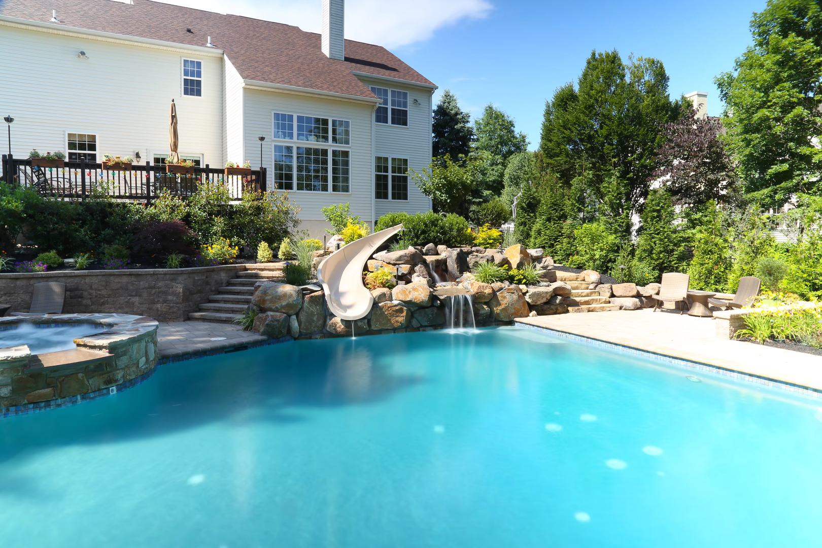 Multi-tiered natural stone waterfall cascading into a backyard pool surrounded by lush plants
