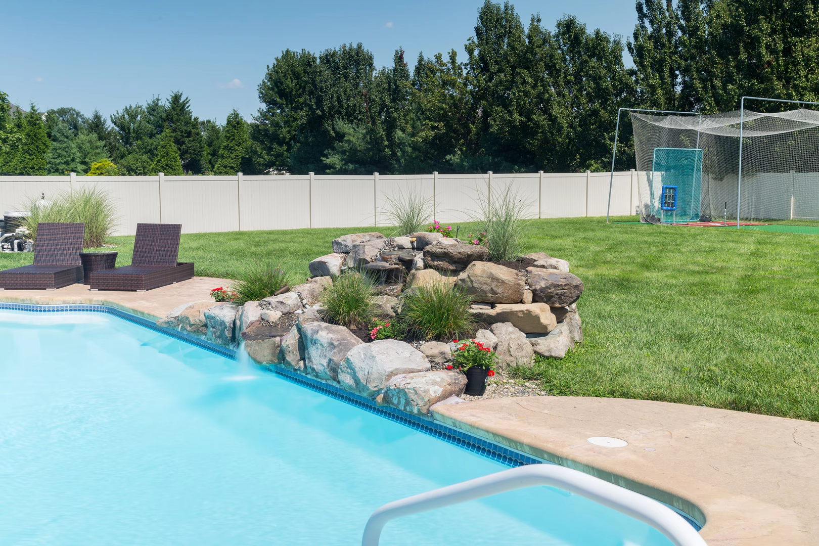 Multi-tiered natural stone boulder waterfall cascading into a pool bordered by ornamental grasses and flowers
