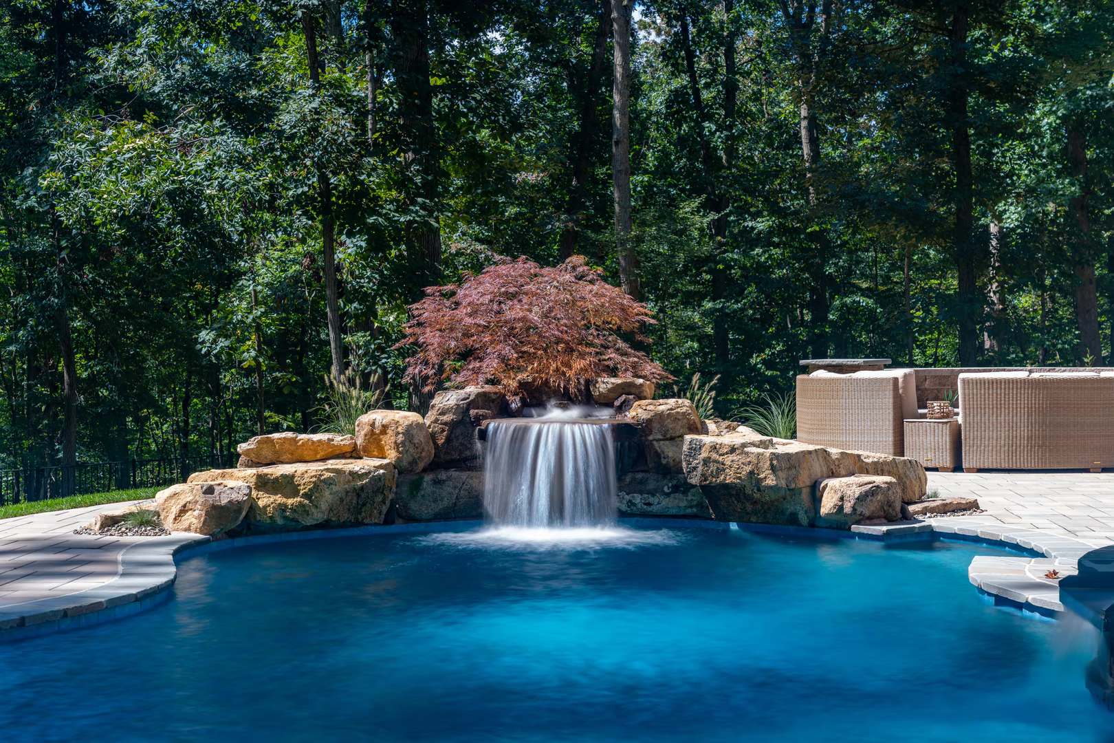 Single-tier natural stone boulder waterfall cascading into a pool with a red Japanese maple