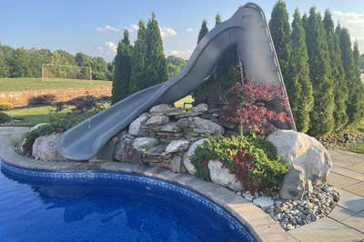 Chania A - Hamilton, NJ - A water slide in the middle of a swimming pool surrounded by rocks and plants