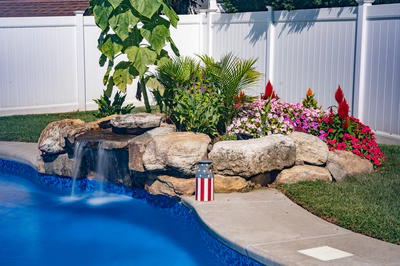 Chapel E - West Long Branch - A backyard with a pool and a waterfall surrounded by flowers and greenery