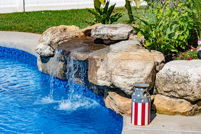 Chapel F - West Long Branch - A blue swimming pool with a waterfall in the middle surrounded by rocks and flowers
