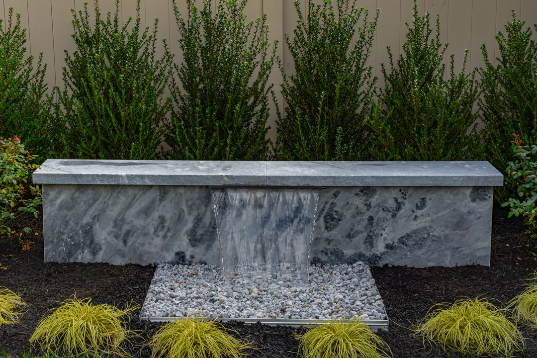 Formal G -  - A concrete bench with a waterfall in a garden setting surrounded by shrubs and grasses