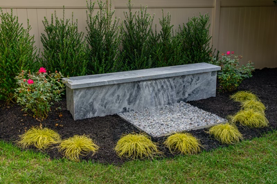 Formal G -  - A concrete bench with a waterfall in a garden setting surrounded by plants and flowers