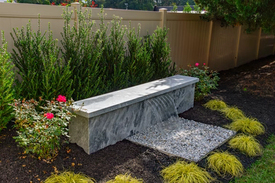 Formal G -  - A concrete bench with a waterfall in a garden setting surrounded by plants and flowers