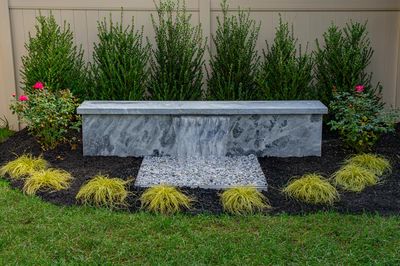 Formal G -  - A concrete bench with a waterfall in a garden setting surrounded by plants and grass