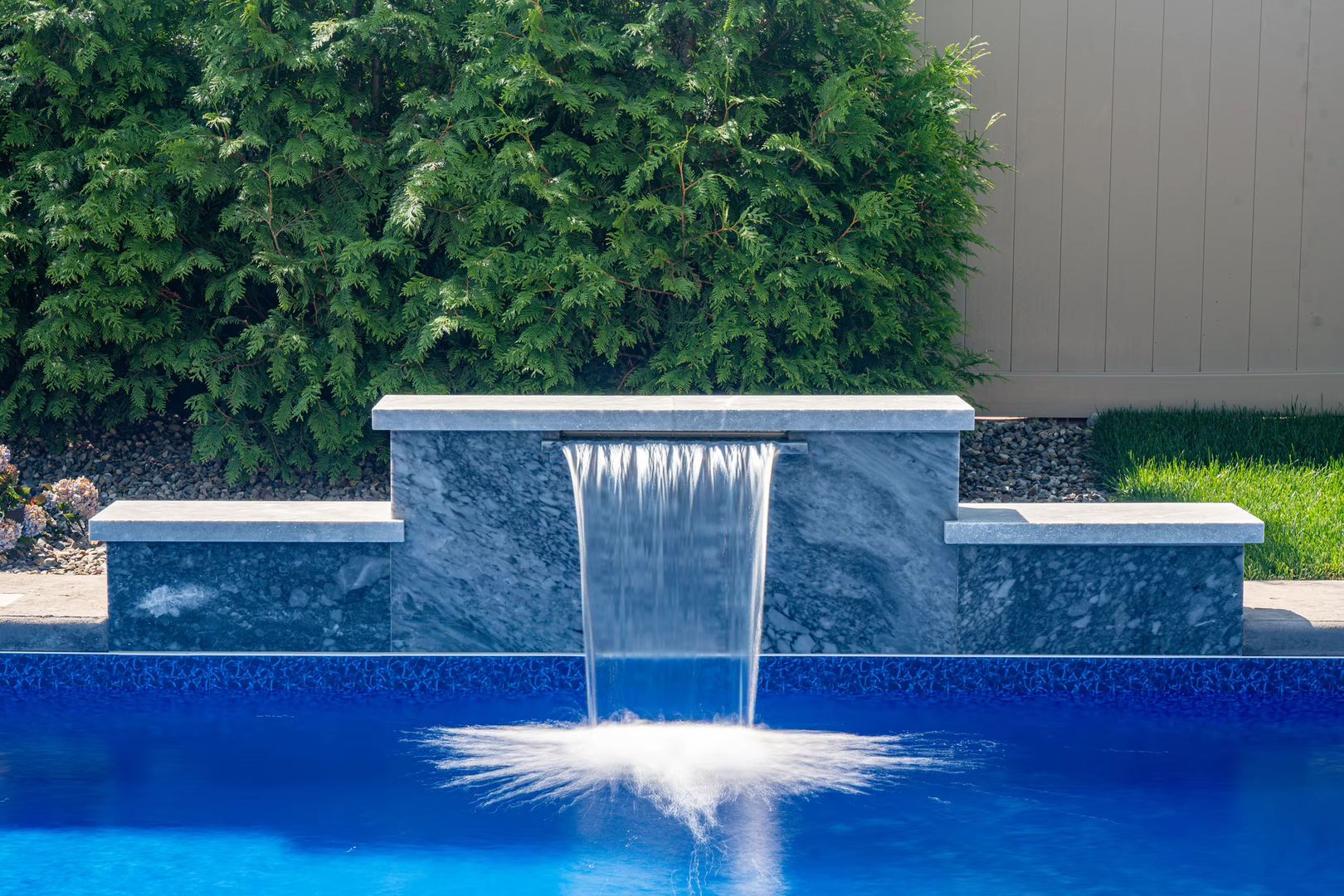 Three-tiered natural stone wall featuring sheer descent waterfall spilling into pool with lush hedges