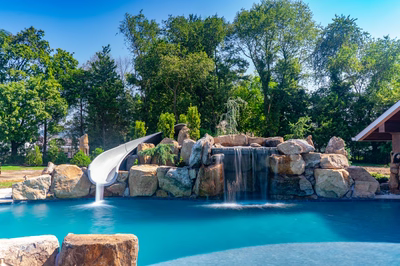Cispus A - Mantua, NJ - A swimming pool with a waterfall and a water slide surrounded by lush greenery