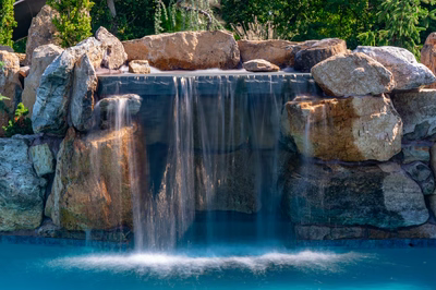 Cispus D - Mantua, NJ - A large rock waterfall in the middle of a swimming pool surrounded by lush greenery