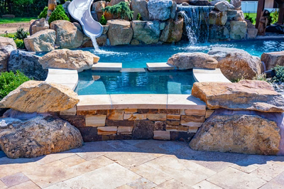 Cispus O - Mantua, NJ - A swimming pool with a waterfall and a slide surrounded by rocks and plants