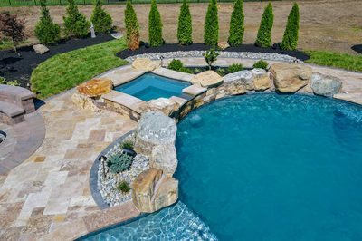 Cispus S - Mantua, NJ - A swimming pool with a waterfall feature surrounded by lush greenery and stone pavers