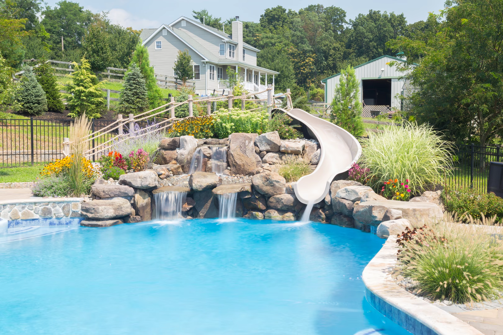 Multi-tiered natural stone boulder waterfall cascading into a pool surrounded by lush garden plants