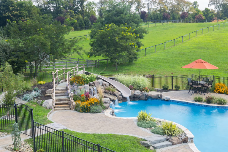 Natural stone boulder waterfall cascading into a pool surrounded by lush garden plants