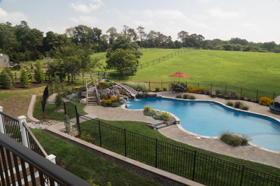 Clarendon F - Cream Ridge, NJ - A backyard with a swimming pool and a water feature surrounded by lush green grass and trees