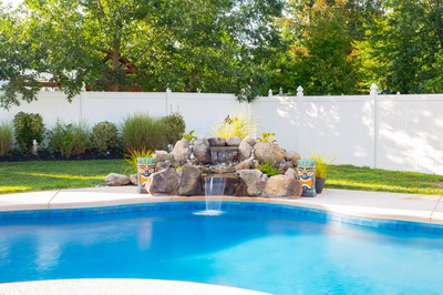Clearwater A - Hainesport, NJ - A backyard with a pool and a waterfall feature surrounded by lush greenery